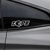 A white stylized DOPE decal sticker is placed on the dark tinted window of a car.