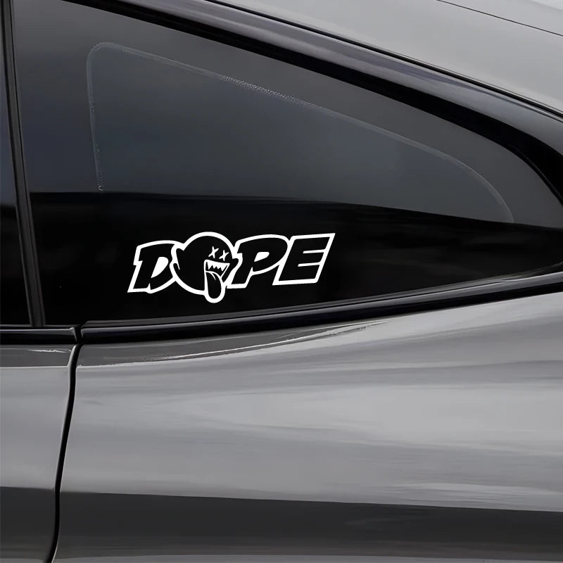 A white stylized DOPE decal sticker is placed on the dark tinted window of a car.