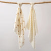 A set of two white baby gauze swaddle blankets tied on a wooden branch.