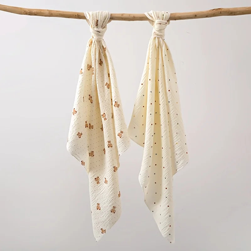 A set of two white baby gauze swaddle blankets tied on a wooden branch.