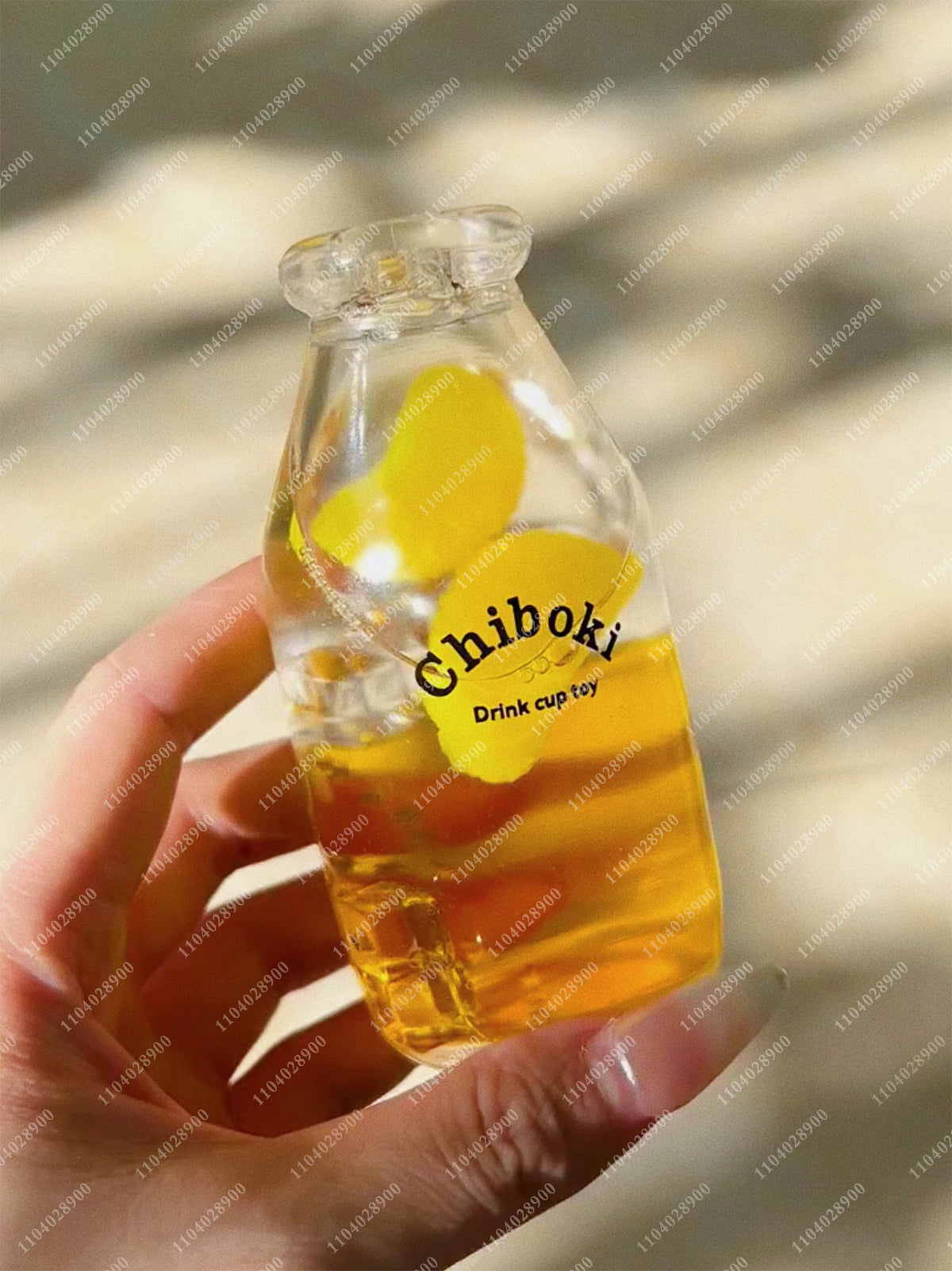 A hand holds a clear glass bottle filled with yellow liquid and floating yellow rubber toys for sensory relaxation.
