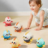 A smiling toddler is interacting with several ceramic wind-up chick toys of various colors on a light surface.