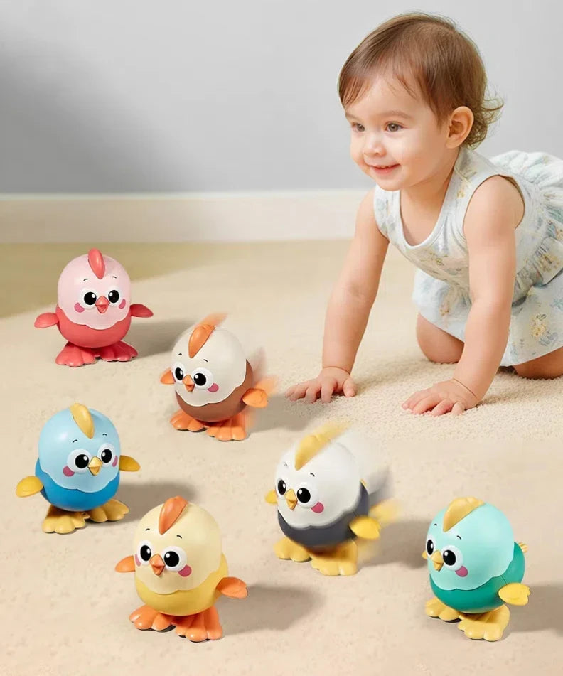 A smiling toddler is interacting with several ceramic wind-up chick toys of various colors on a light surface.