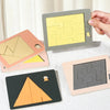 A hand holds a light gray wooden geometric brain teaser puzzle with a yellow maze pattern, next to other puzzles.