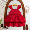 A red pleated dress for a baby girl displayed on a wooden hanger in front of a mirror.