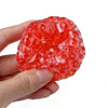 A hand holds a translucent red mochi squeeze toy, which is a soft fidget ball for stress relief.