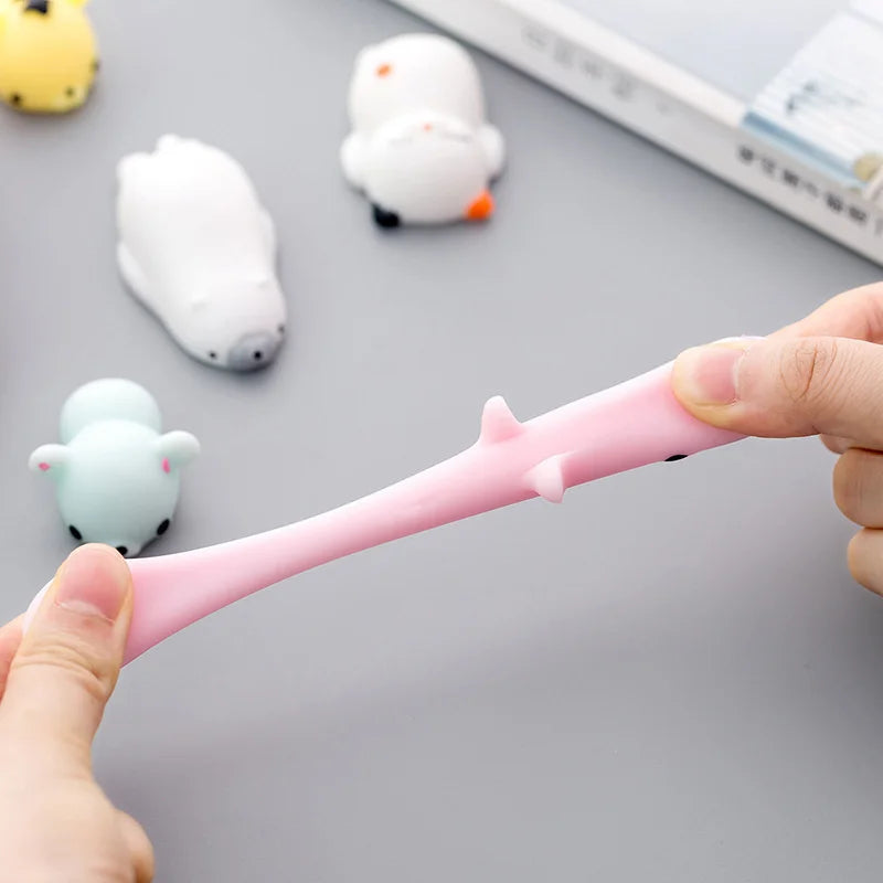 A hand is squeezing a pink squishy toy shaped like a pink pig among other white and orange animal stress relief balls.