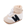 A pair of beige and white ankle-hugging baby booties with a knit cuff and anti-slip sole.