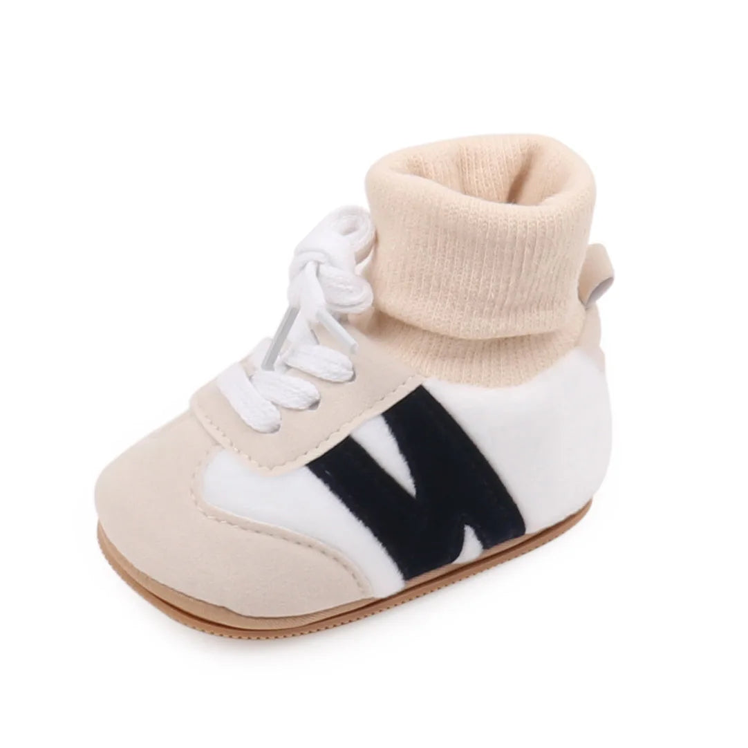 A pair of beige and white ankle-hugging baby booties with a knit cuff and anti-slip sole.