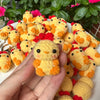 A hand holds a yellow crochet chick keychain, surrounded by many similar orange and yellow crocheted animals.