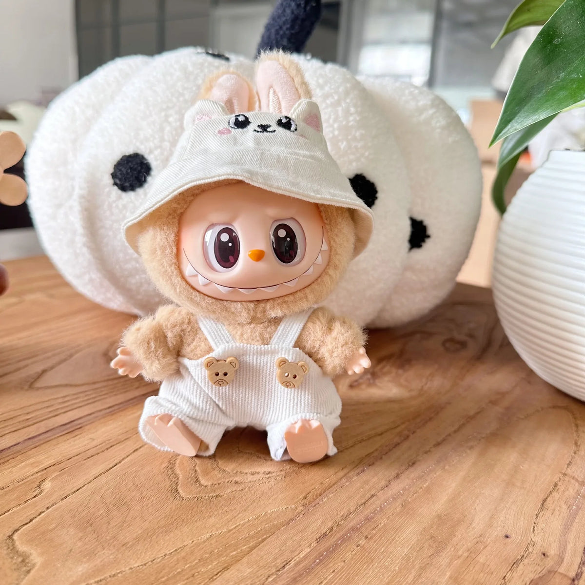 A Labubu doll wearing a beige hoodie and headphones, sitting in front of a large white fluffy object.