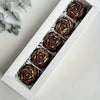 A white box filled with six dark chocolate rosette leaves for cake and chocolate decorating.