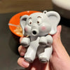 A small, gray elephant figurine is held in a hand above an orange plate.