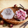 A pink floral silicone candle and resin mold rests in a woven basket surrounded by dried roses and lavender.