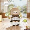 A cute plush keychain of a girl with light brown hair and large eyes wearing a white dress and brown bow, holding a green ite