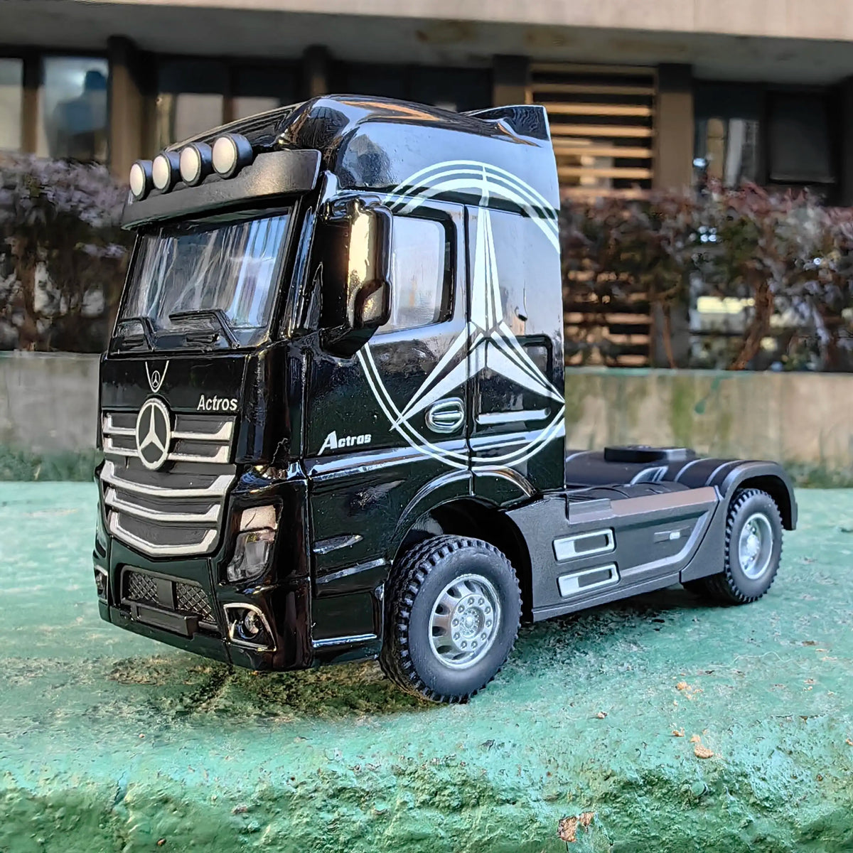 A black Mercedes-Benz Actros diecast truck with lights parked on a green surface.