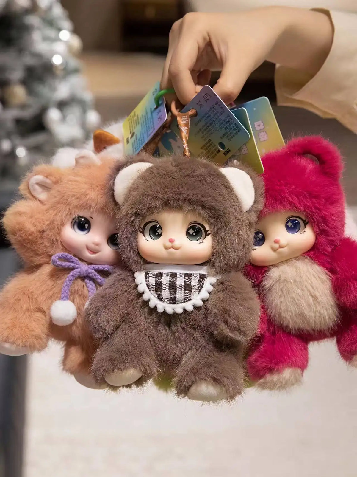 A hand is holding three plush animal pendants: a brown rabbit, a gray bear, and a pink sheep.