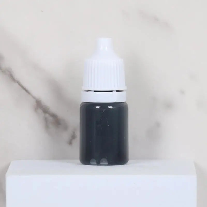 A black dropper bottle with a white cap sits on a white surface.