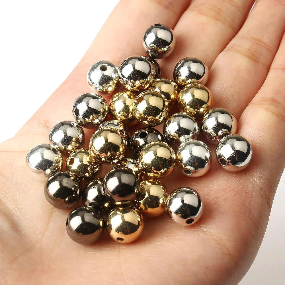A hand holds a cluster of round spacer beads in gold and silver tones for DIY jewelry making.