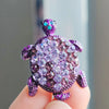 A purple rhinestone turtle brooch pin held between fingers.