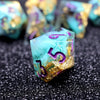 A close-up of a translucent teal resin die with purple numbers and gold glitter, resting on a dark surface.