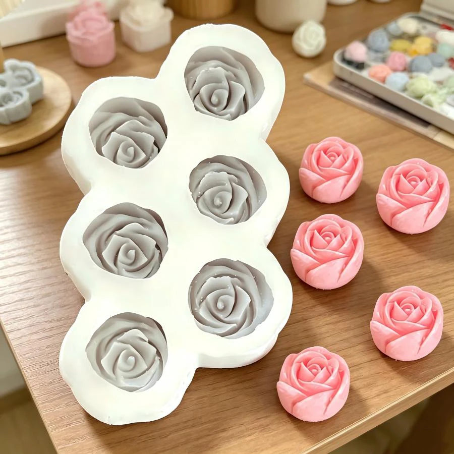A white silicone mold set featuring multiple 3D rose flower shapes in various shades of pink and gray.