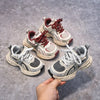 A hand holds a pair of red and white breathable mesh kids running sneakers with cushioned soles.
