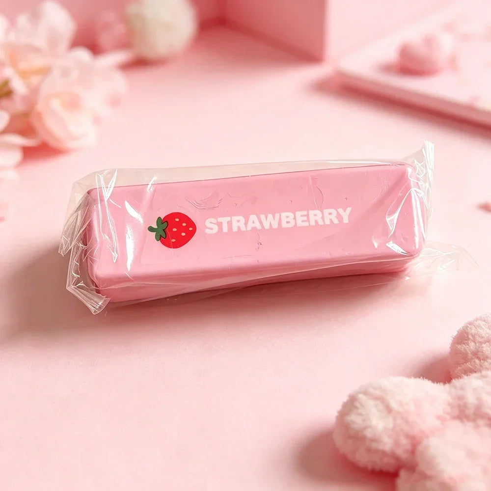 A pink strawberry shaped squishy fidget toy packaged in a clear plastic bag on a light pink surface.