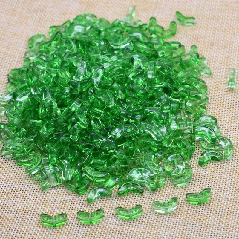 A pile of bright green tulip flower glass beads scattered on a light brown fabric surface.