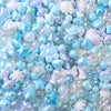 A close-up of iridescent blue and purple acrylic bow beads scattered on a white surface.