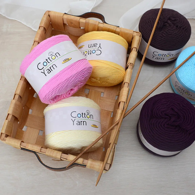 A wooden basket filled with various skeins of yellow, pink, purple, and blue cotton yarn.