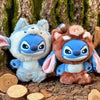 A plush collectible pendant of Stitch featuring pink and blue fur and large ears resting on a wooden surface.
