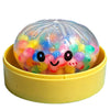 A clear plastic squishy toy filled with colorful glitter and bubble-like spheres resting in a yellow container.