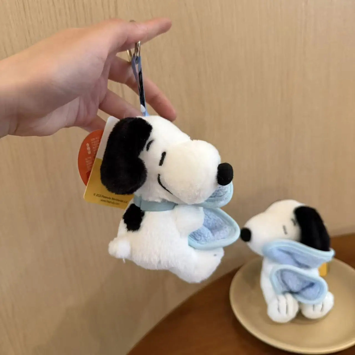 A white Snoopy plush keychain charm is being held by a hand against a light background.