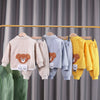 A set of kids' cartoon bear corduroy tracksuit jacket and pants hanging on a wooden rack.