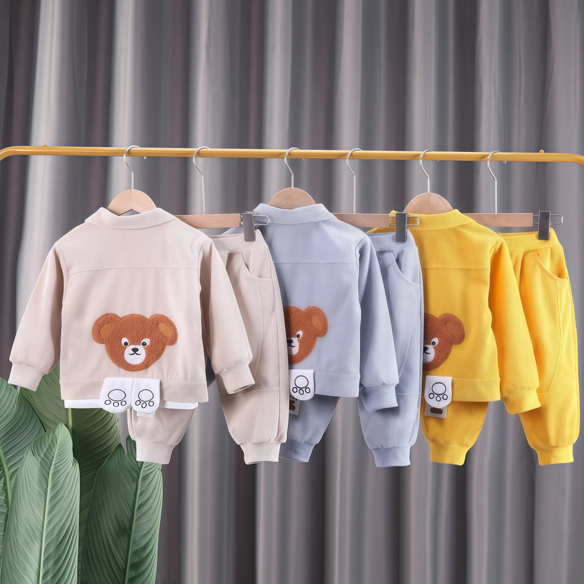A set of kids' cartoon bear corduroy tracksuit jacket and pants hanging on a wooden rack.
