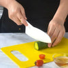 A hand is using a white plastic knife to cut a cucumber on a yellow cutting board.