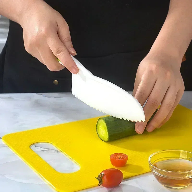 A hand is using a white plastic knife to cut a cucumber on a yellow cutting board.