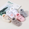 A collection of handmade knitted baby booties in white, pink, and gray with animal designs displayed next to a book.