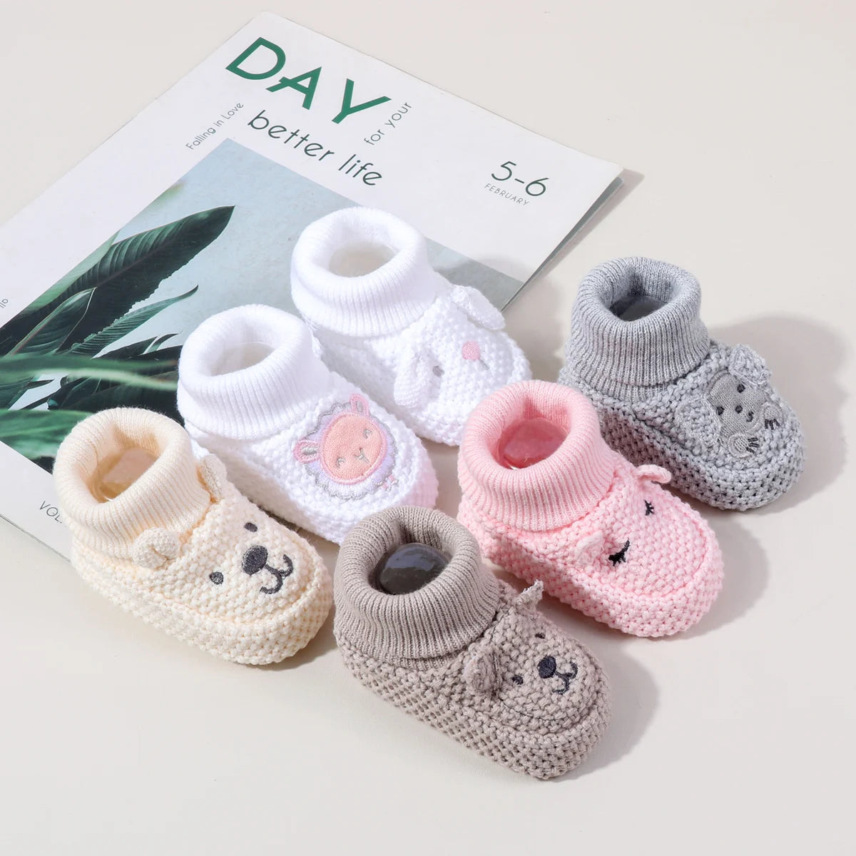 A collection of handmade knitted baby booties in white, pink, and gray with animal designs displayed next to a book.