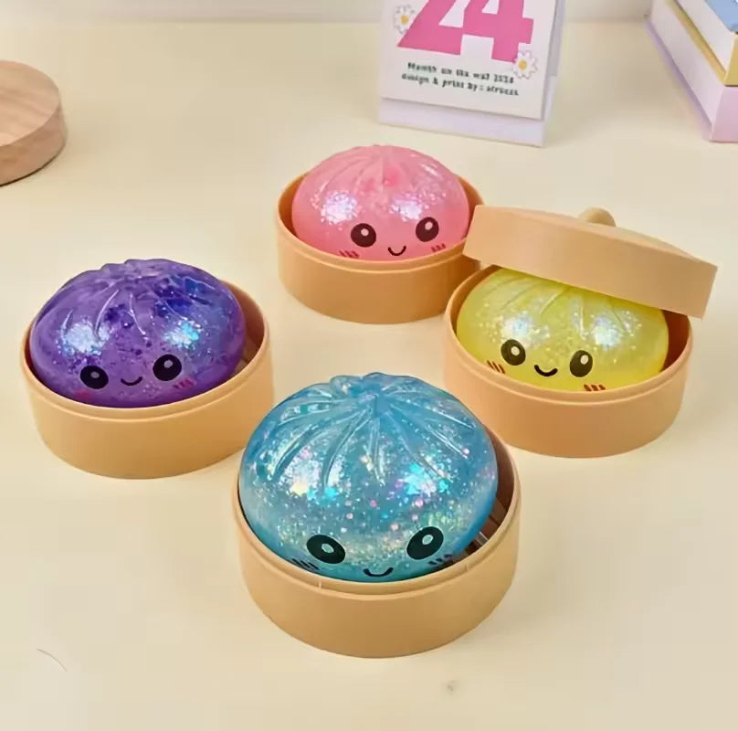 A collection of four squishy glitter steamed bun fidget toys in pink, yellow, purple, and blue are displayed in light brown c