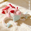 A pink and white rainbow dragon plush toy lying on a fluffy cream-colored surface.