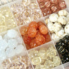 Assortment of gold and white pumpkin resin beads for jewelry making displayed in small compartments.