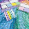 A collection of colorful putty wax blocks and diamond painting pens are displayed on a textured, multicolored surface.
