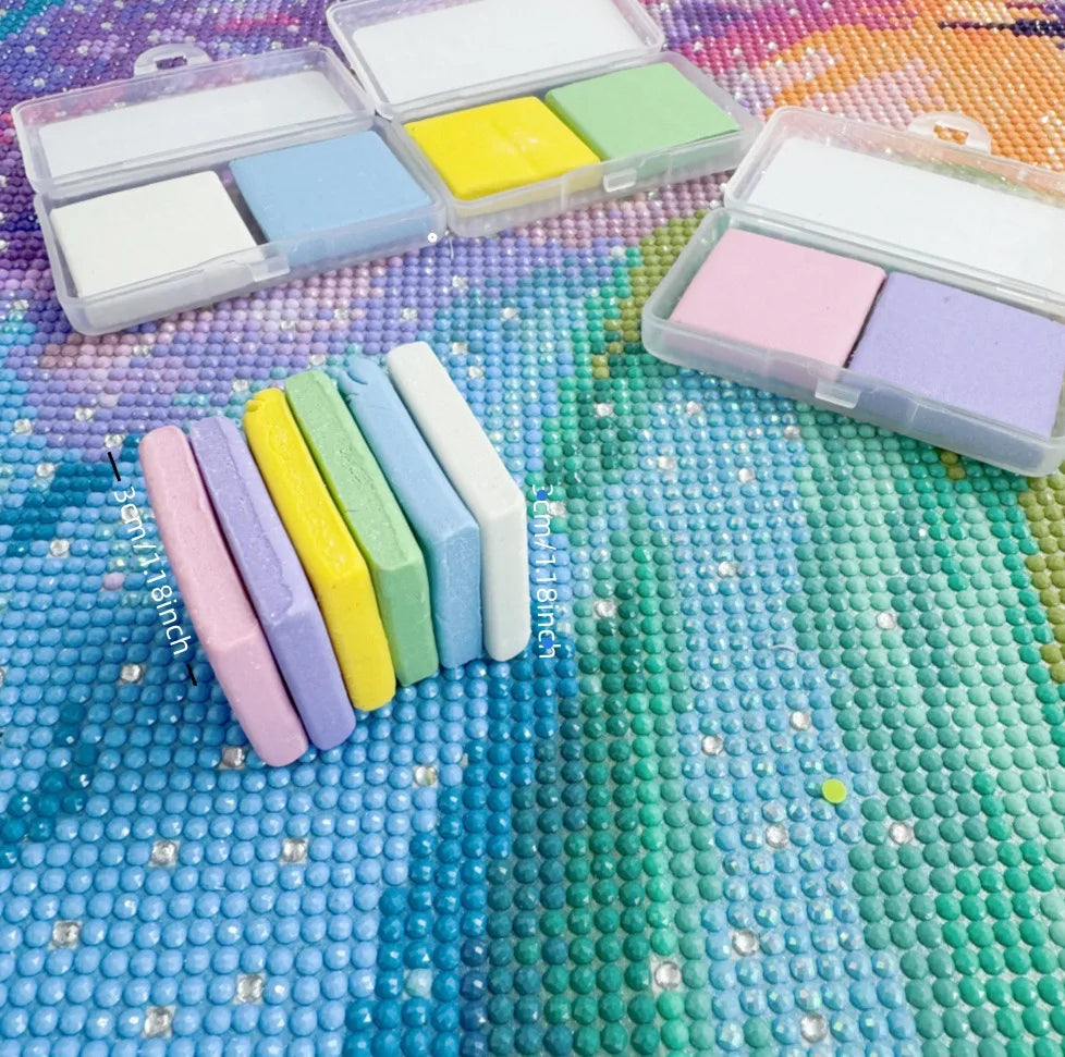 A collection of colorful putty wax blocks and diamond painting pens are displayed on a textured, multicolored surface.