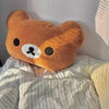 A brown Rilakkuma soft plush hand rest pillow resting on striped bedding.