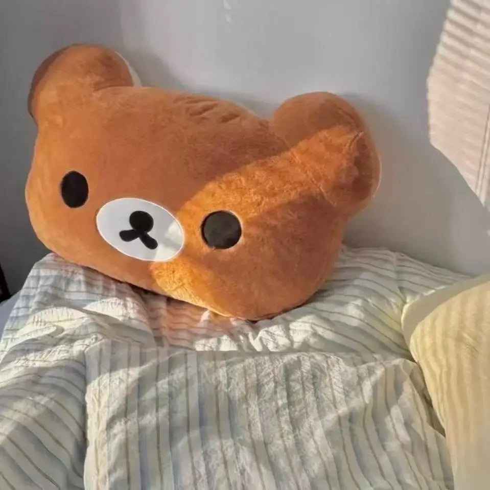 A brown Rilakkuma soft plush hand rest pillow resting on striped bedding.