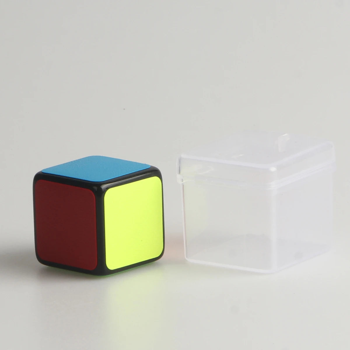 A mini magic cube puzzle with black, red, and neon yellow faces is shown on a white surface.