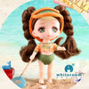 A small orange-haired doll with brown hair and green eyes standing on sand, featuring poseable joints.