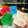 A hand holds a clear, translucent green squishy toy cube on a white plate.